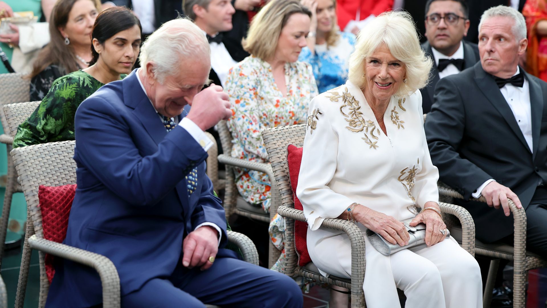 King Charles and Queen Camilla laughing while sitting in chairs
