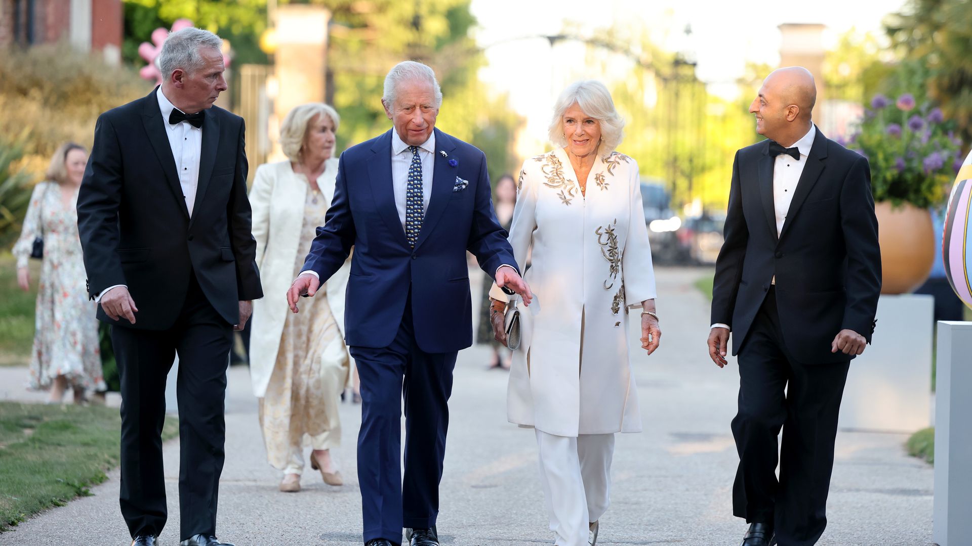 King Charles and Queen Camilla walking with two men in tuxedos