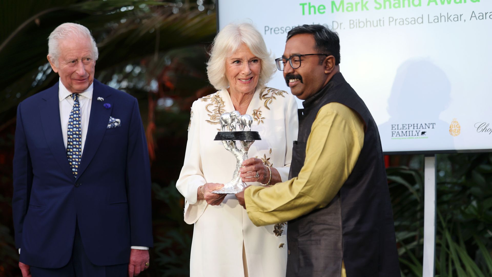 Queen Camilla handing over an award with King Charles standing by her