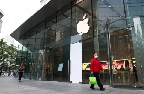 EPA Woman wearing a red jacket and mask walks past an Apple store in Beijing on 12/5/2025