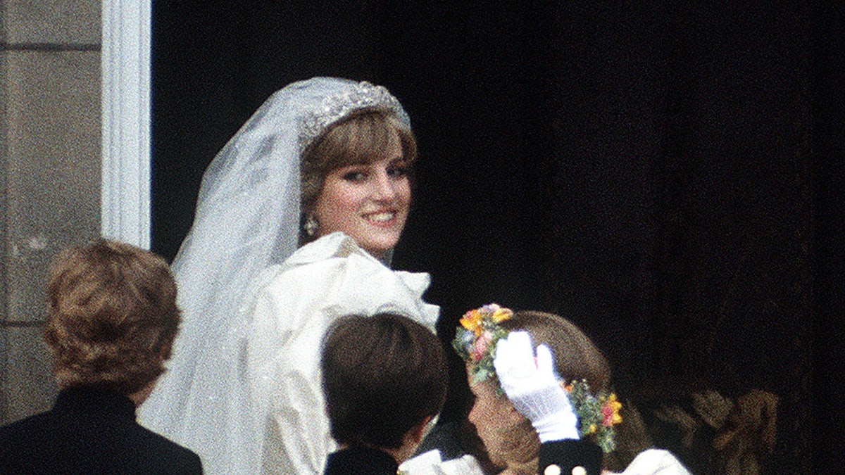Princess Diana smiling wearing her bridal gown with children in front of her.