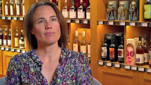 Annabel Thomas sitting in front of rows or bottles of whisky on shelves