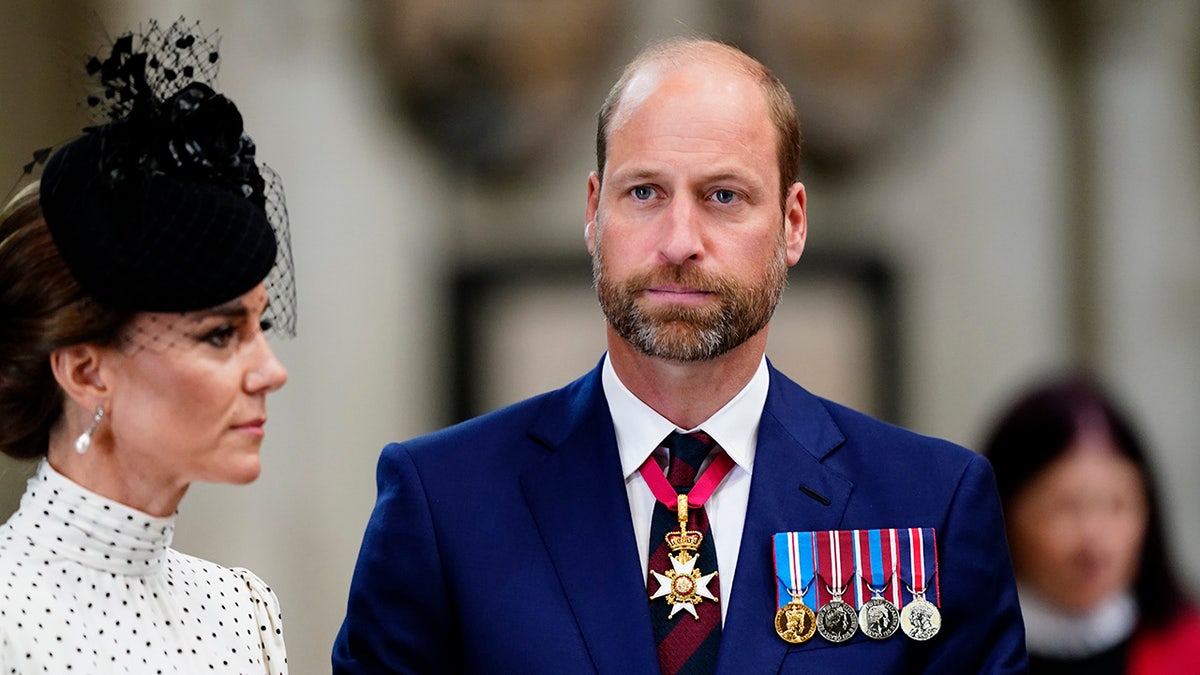 Kate Middleton in a polka dot dress and black fascinator looking to the side as Prince William in a dark blue suit and medals looks straight on.
