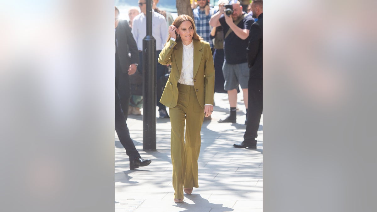 Kate Middleton being photographed in an olive suit outdoors.