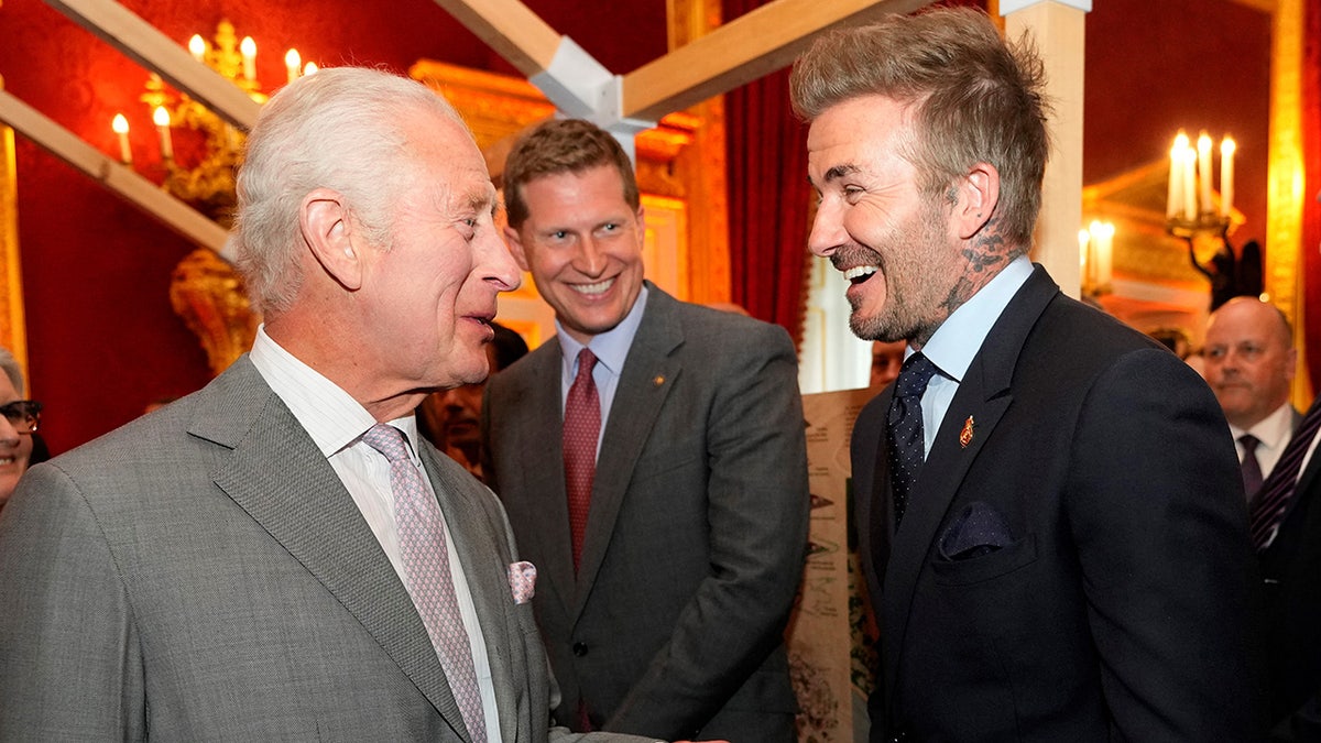 King Charles and David Beckham smiling at each other in mid conversation.