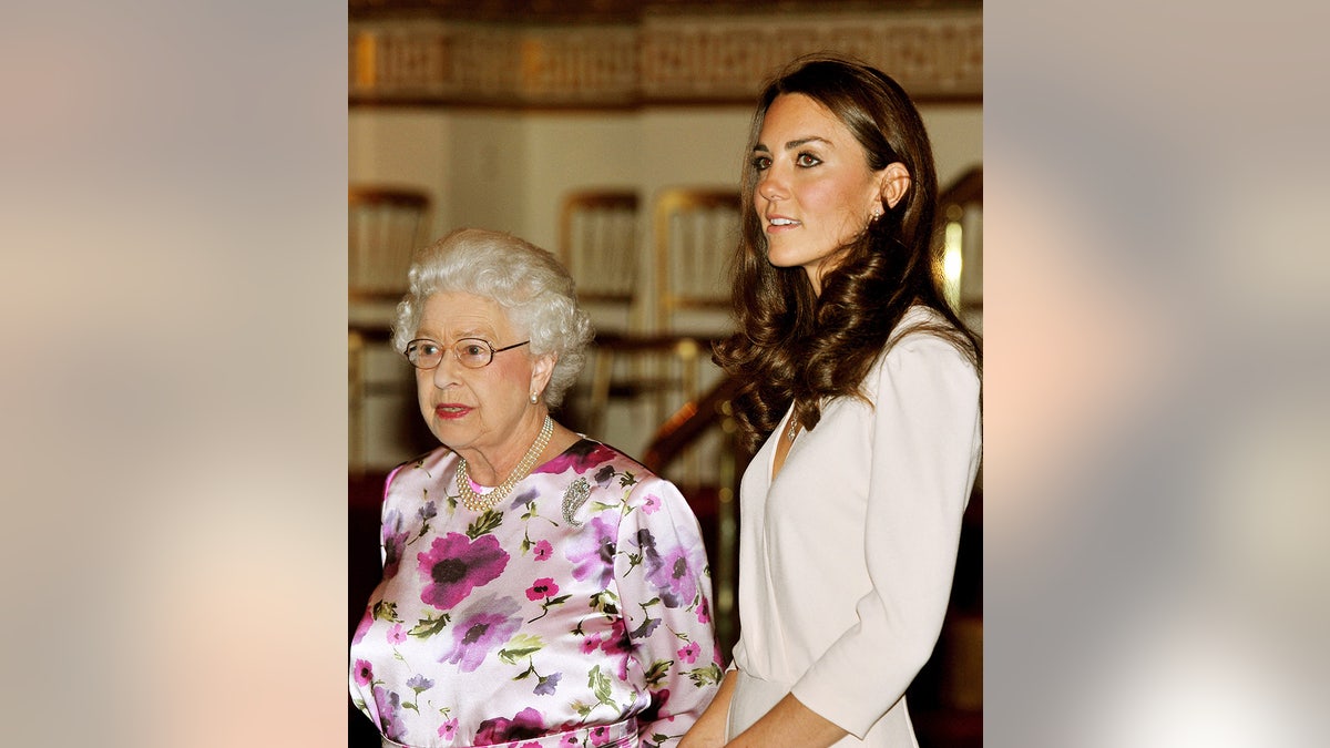 Kate Middleton in a beige dress next to Queen Elizabeth in a purple floral dress.