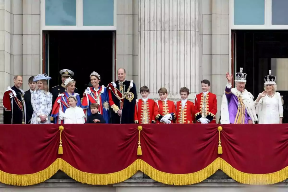 A group of people dressed in formal and colorful suits is on a balcony decorated with red and gold curtains in front of a building with columns.