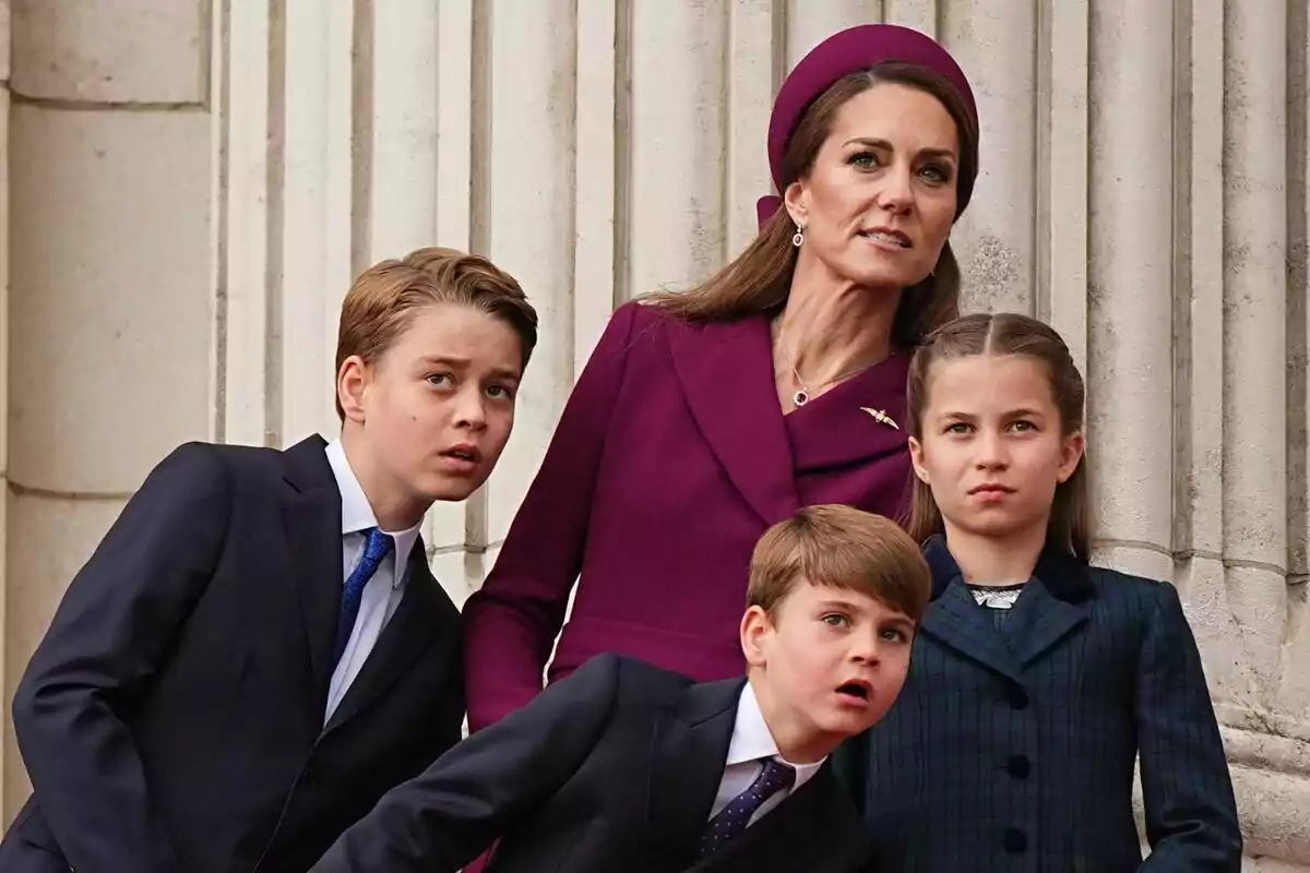 A woman and three children dressed formally look up with expressions of interest in front of a building with columns.