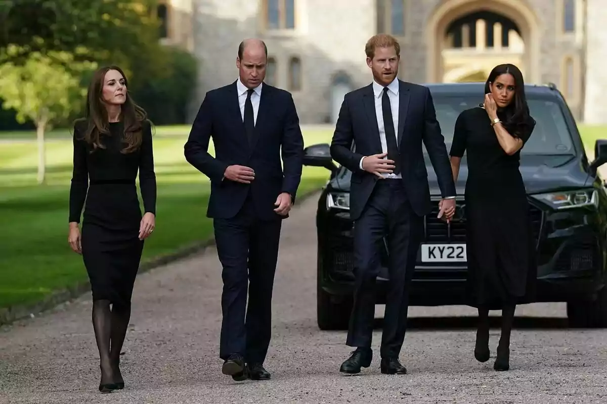 Four people dressed in black walking on a gravel path with a historic building in the background.