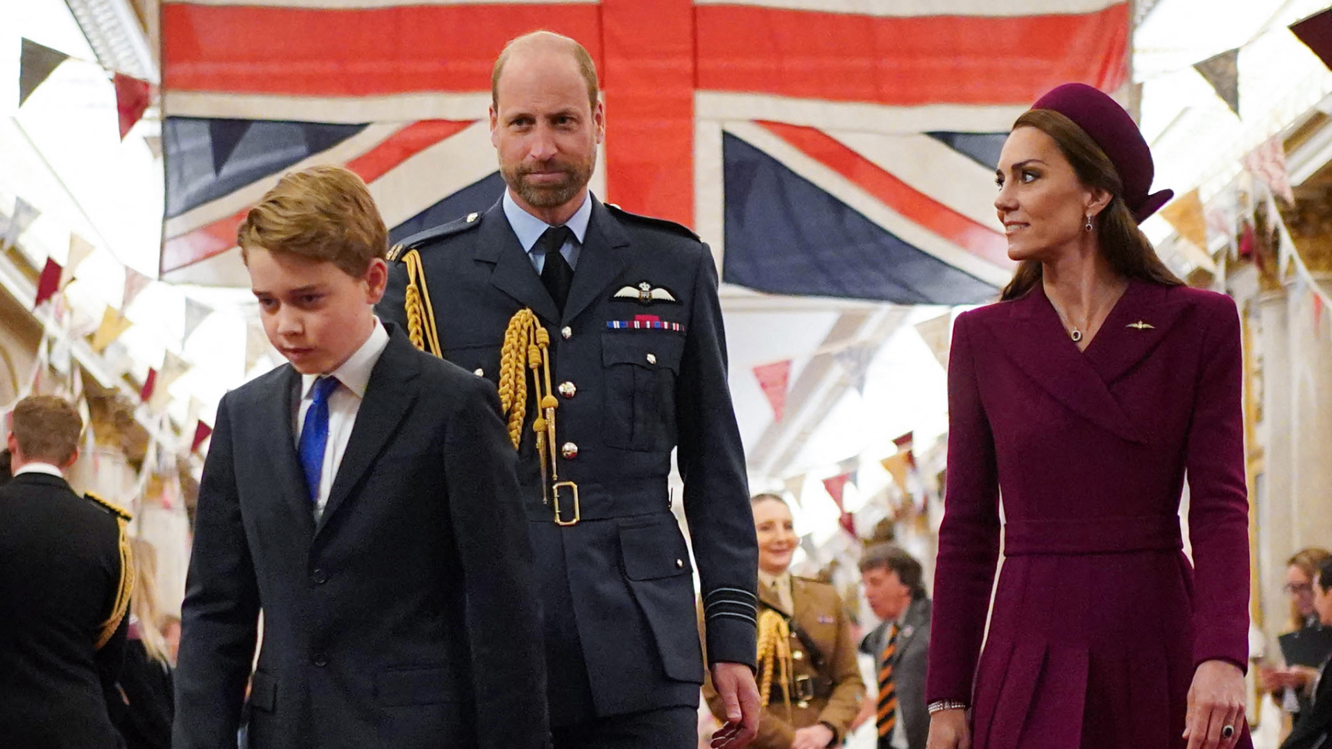 Princess Kate, Prince George, Prince William walking in front of a Union Jack