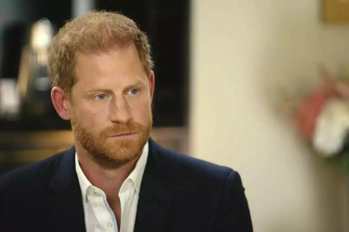 Prince Harry dressed in a dark suit and white shirt, sitting in an indoor setting.