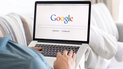 Getty Images Person sitting on a couch searching Google on a laptop 