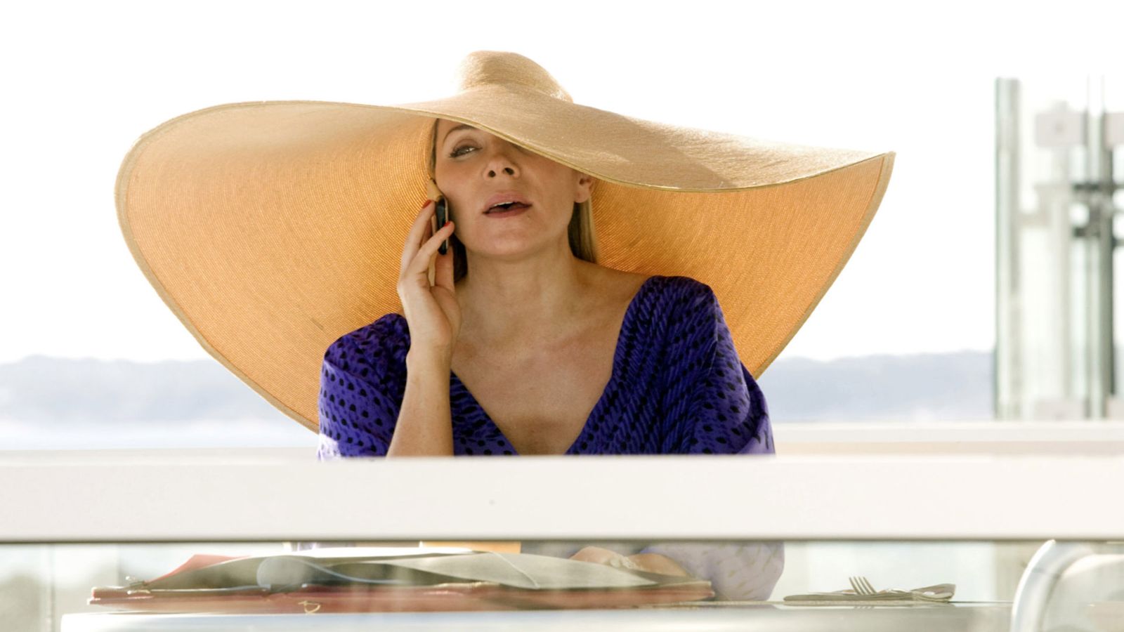 Image may contain Kim Cattrall Clothing Hat Sun Hat Adult Person Cutlery Fork Electronics Mobile Phone and Phone