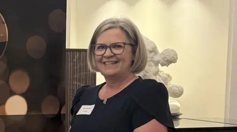 Cybermindz Lisa Ackerman, wearing a smart black top, smiles while standing in front of a classical scuplutre.