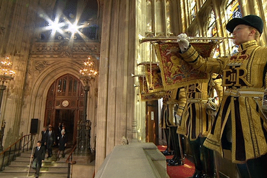 Trumpeters in ceremonial uniform play as people enter a grand hall.