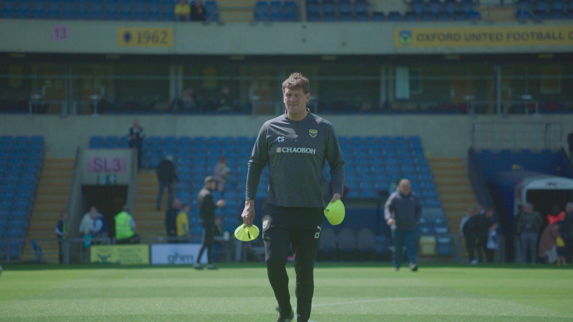Craig Short standing in the middle of the pitch at Oxford United's stadium laying out cones for training.