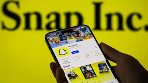 Getty Images Snapchat's Apple App Store listing displayed on an iPhone, held in a person's palm, against a yellow background.