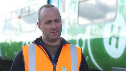 University of Birmingham Wearing an orange hi-vis vest Stuart Hillmansen stands in front of a railway carriage.