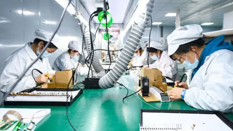 Getty Images In a semiconductor factory in China, workers on a production line rush to assemble liquid crystal displays and modules. The image shows at least five workers using soldering pens to work on the screens