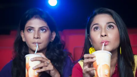 Getty Images Two women having soft drinks while watching movie in a cinema hall