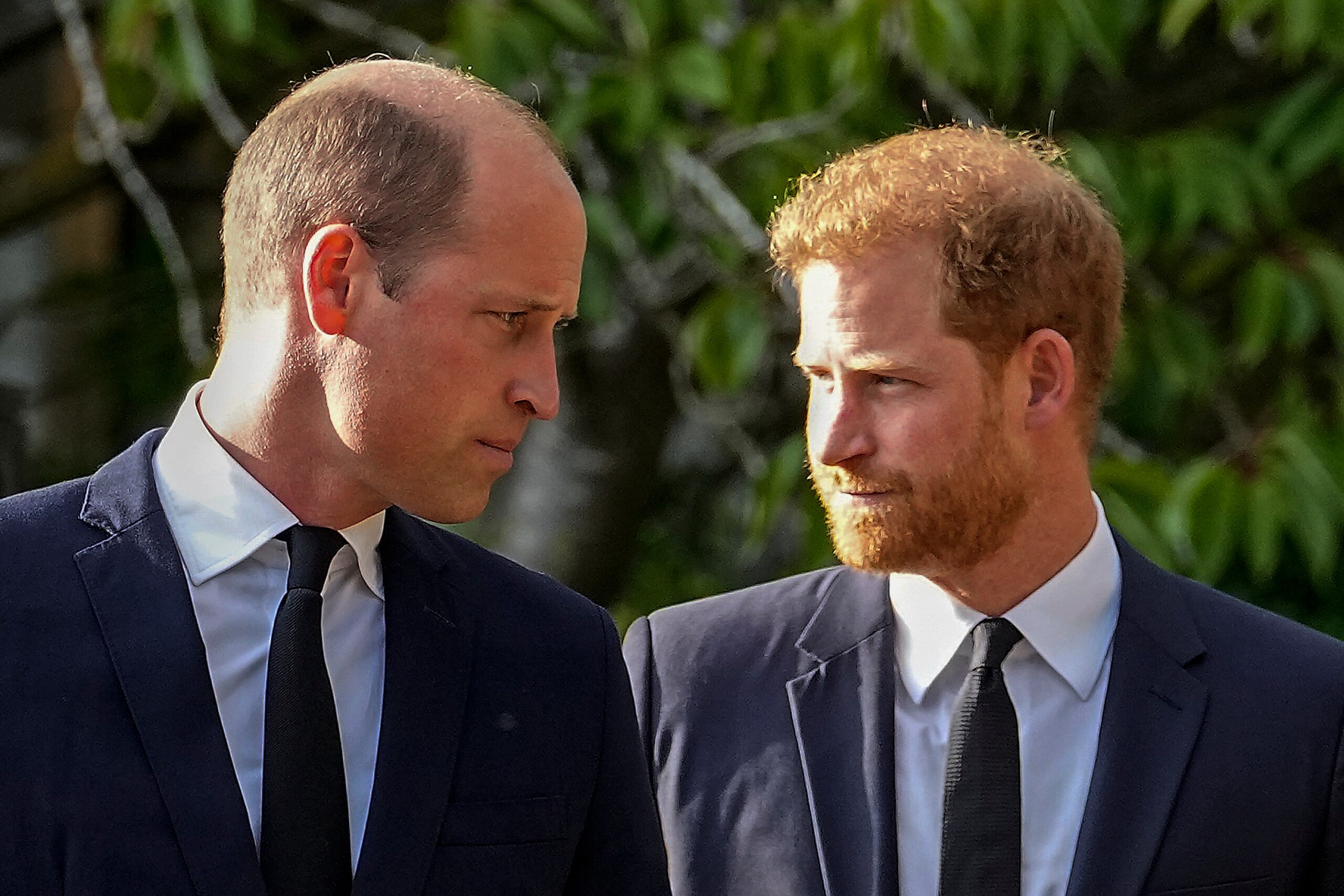 Princes William and Harry in suits, walking together outside Windsor Castle.