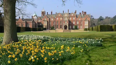 Getty Images A view of The Church of St Mary Magdalene on Sandringham estate. Daffordils, a lush lawn and a tree are in the foregrounf of the large red-bricked building.