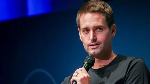 Bloomberg via Getty Images Snap boss Evan Spiegel shown looking away from the camera to his left as he speaks into a microphone on-stage at an event.