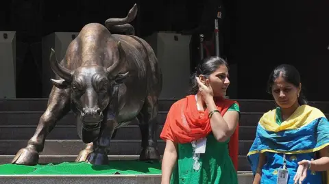 Getty Images Indian women walk past the bronze bull outside the Bombay Stock Exchange, wearing traditional salwar-kurtas.