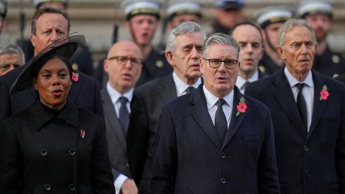Kemi Badenoch and Keir Starmer standing in front of David Cameron, Gordon Brown and Tony Blair. They are all dressed in dark clothing and wearing poppies