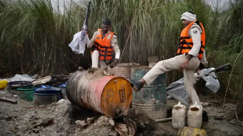 Seraj Ali Two armed officers, standing amid drums and jars on a sugarcane farm, destroy an illegal country-made liquor set up in Bihar. 