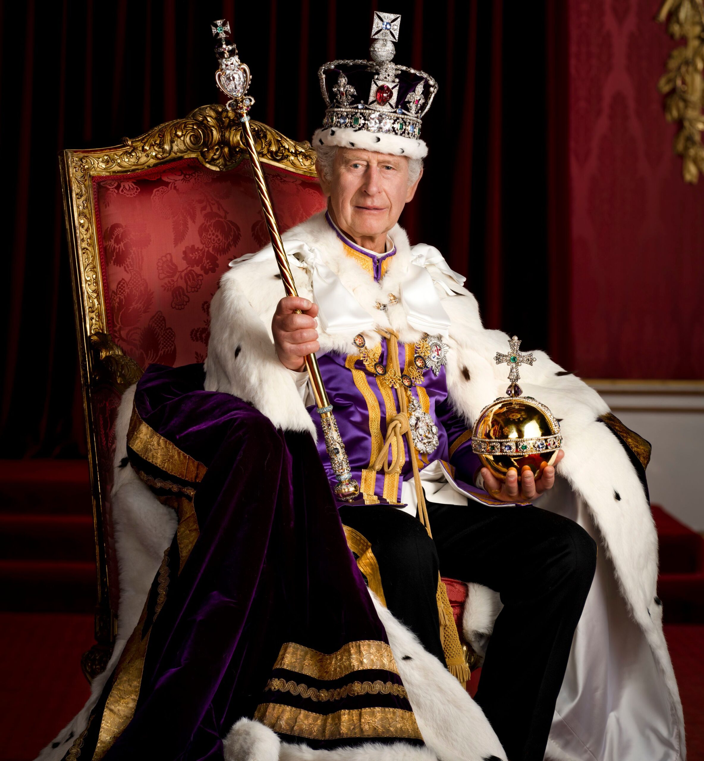 King Charles III in full regalia, wearing the Robe of Estate and Imperial State Crown, holding the Sovereign's Orb and Sceptre, seated on a throne chair.