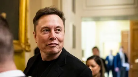 Getty Images Elon Musk wearing a dark jacket. He is looking away from the camera with a smirk on his face