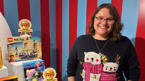 Melissa Symonds stands next to a display of toys and the DreamToys event.