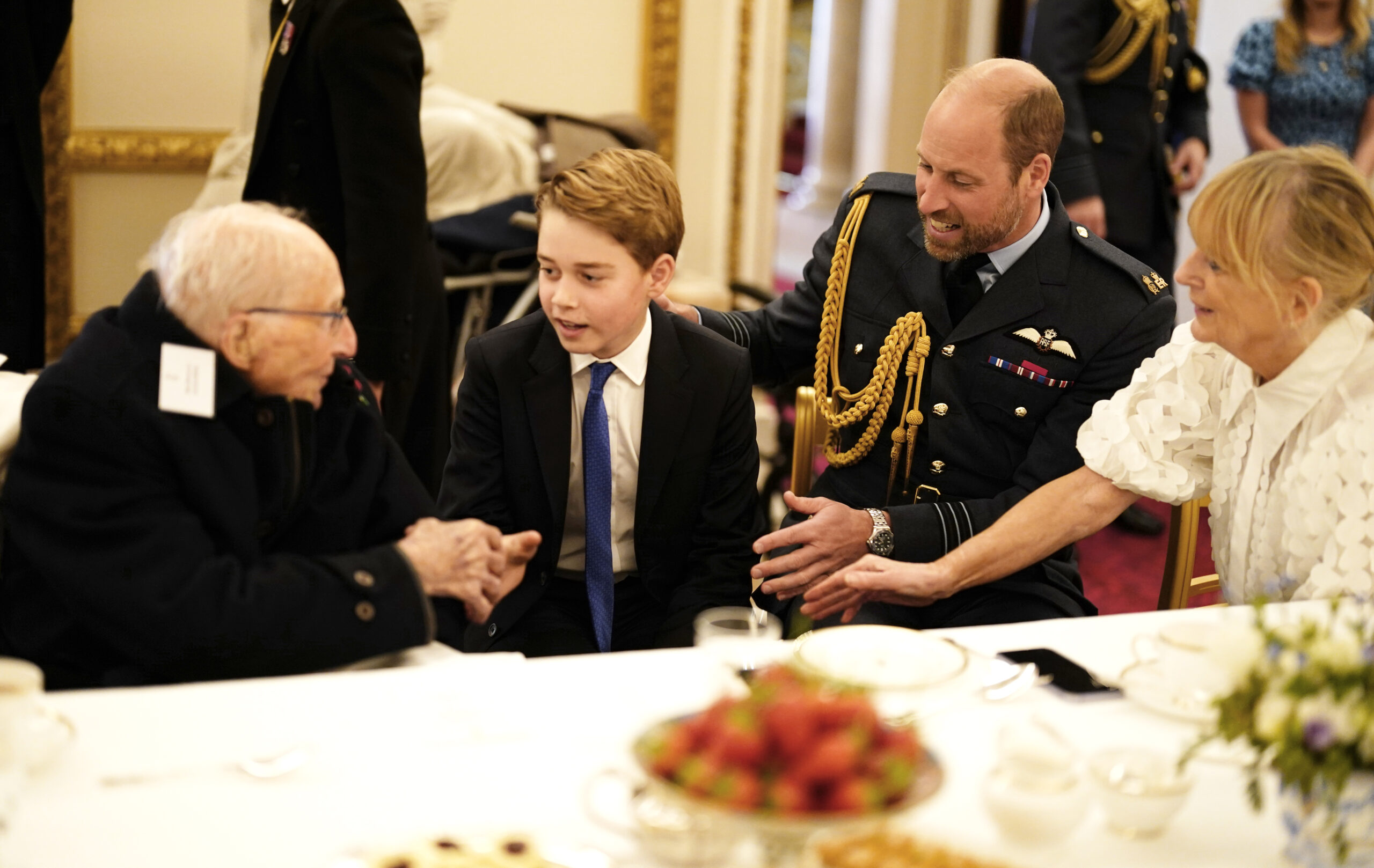 Prince George shaking hands with a veteran, sitting at a table with Prince William