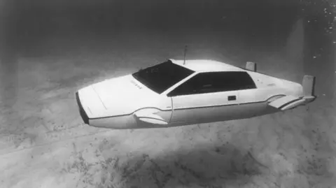 Screen Archives/Getty Images The Lotus Esprit car featured in the 1977 film The Spy Who Loved Me. The white car, featuring protruding fins on its sides and and propellers on its back, is floating underwater near the sea bed, in this black and white image.