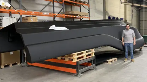 Matthew Kenyon Maarten Logtenberg stands next to the black, upturned hull of a boat in his factory.