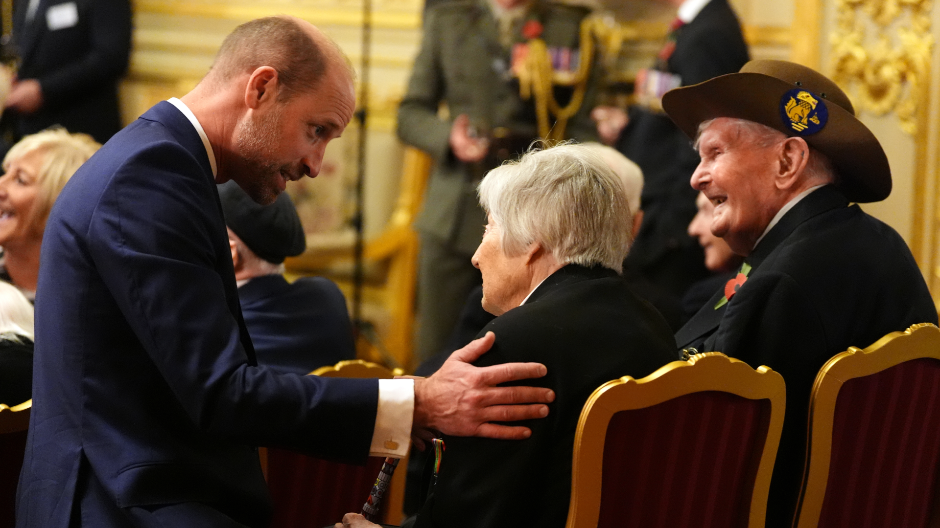 Prince William kneeling and putting his hand on an elderly woman's shoulder