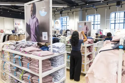 Jason Alden/Bloomberg via Getty Images A woman stands in a Primark store, holding up a hoodie. You can only see her back. She is surrounded by rows of neatly folded clothes