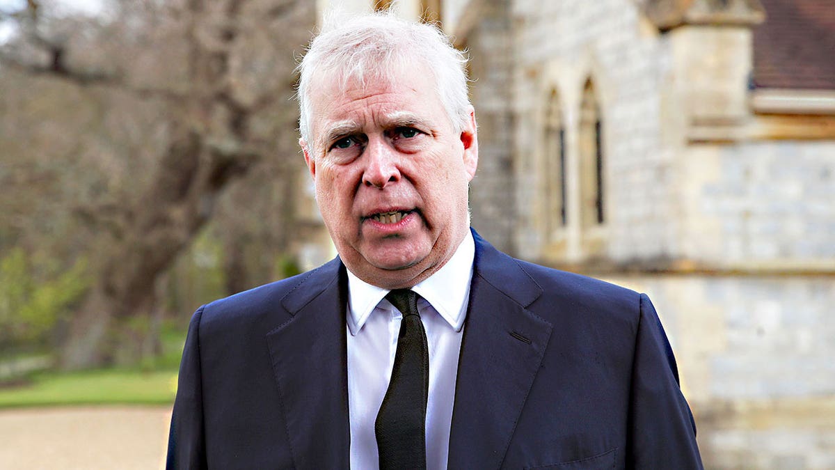 Prince Andrew looking disressed in a dark suit and tie in front of a church.