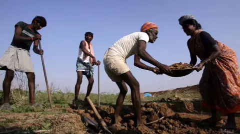 Hindustan Times via Getty Images Three men and a woman pictured with their tools, working on a field. 