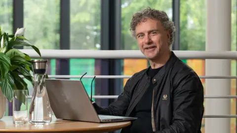 Shaun Scott Wearing a black bomber jacket, Jim Herrington smiles and looks into the camera.