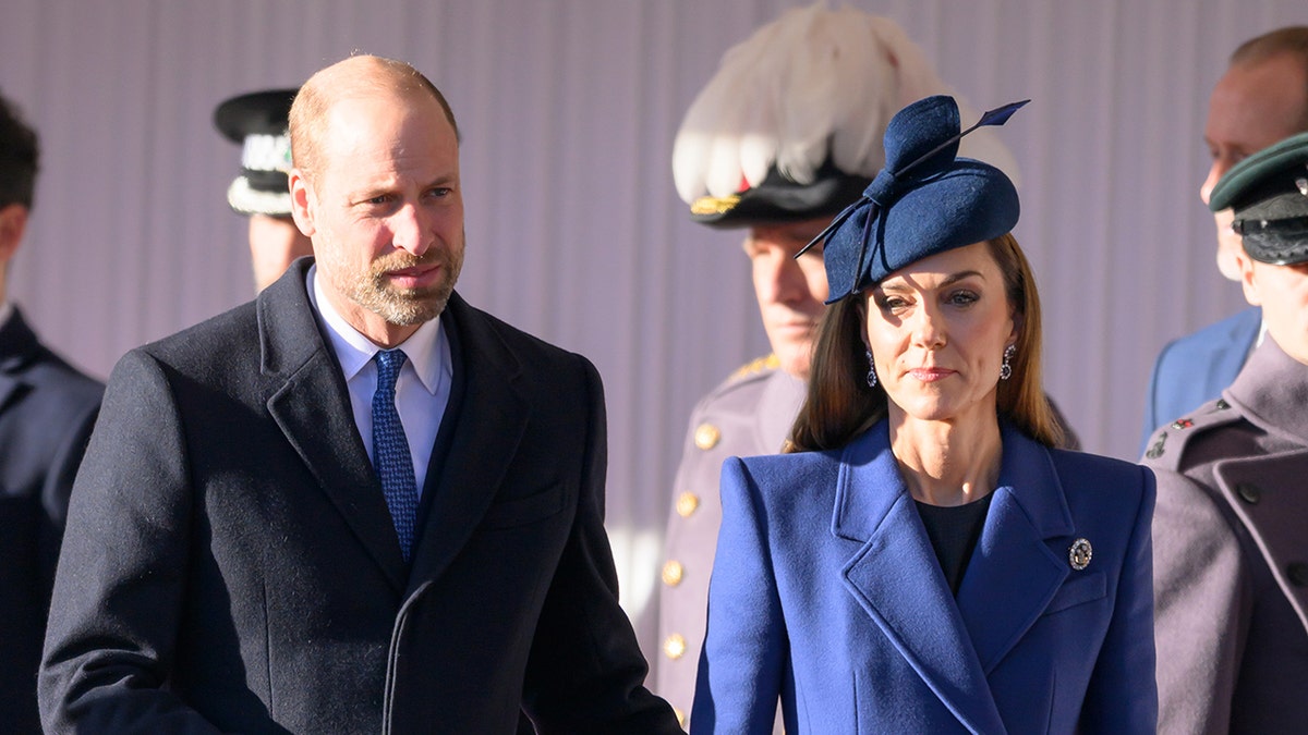 Prince William and Kate Middleton walking together side-by-side outdoors looking serious.