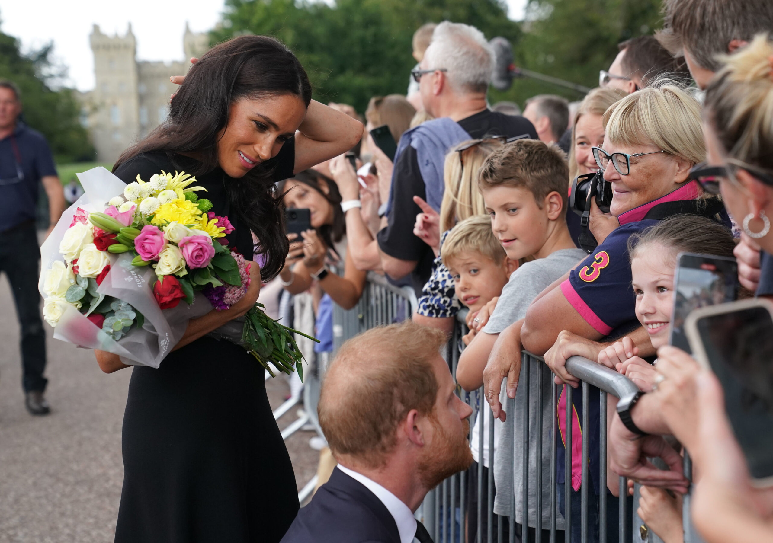Meghan Markle holds a bouquet of flowers as she greets the public while Prince Harry speaks with children at Windsor Castle.
