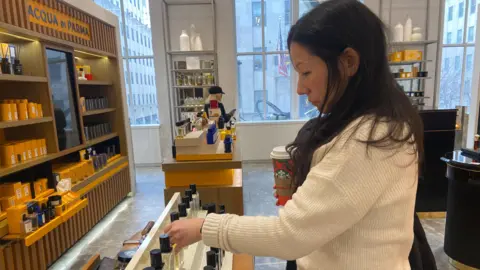 Danielle Kaye/BBC A woman examines fragrance bottles at a department store.