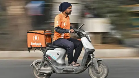 AFP via Getty Images A man, who is a delivery agent with the Swiggy platform, wearing a saffron uniform, rushes on an electric scooter in Bengaluru city on 6 January 2026