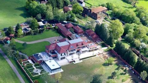 Shutterstock An aerial view of the new mansion at Sunninghill Park, which shows a building in a modern style with white render and a red tile roof. There are large glass doors leading out onto an expansive terrace and at the side of the house is a large flat-roofed, glass-walled building that looks like it may house a swimming pool.