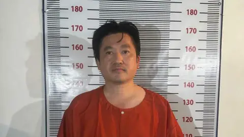 Cambodian Ministry of Information In an orange prison-style uniform, Cambodian businessman Kuong Li stands facing the camera in front of a height-measurement chart