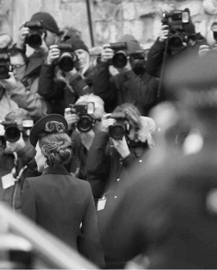 This may contain: black and white photograph of a woman walking in front of a large group of photographers