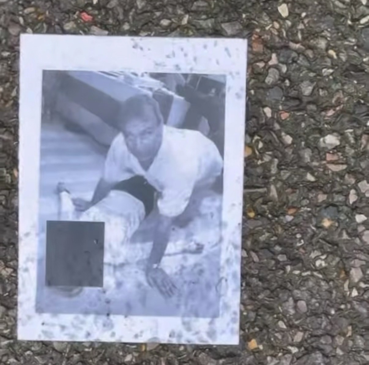 Black and white photo of a man in a t-shirt and shorts, with part of the image obscured, lying on pavement.