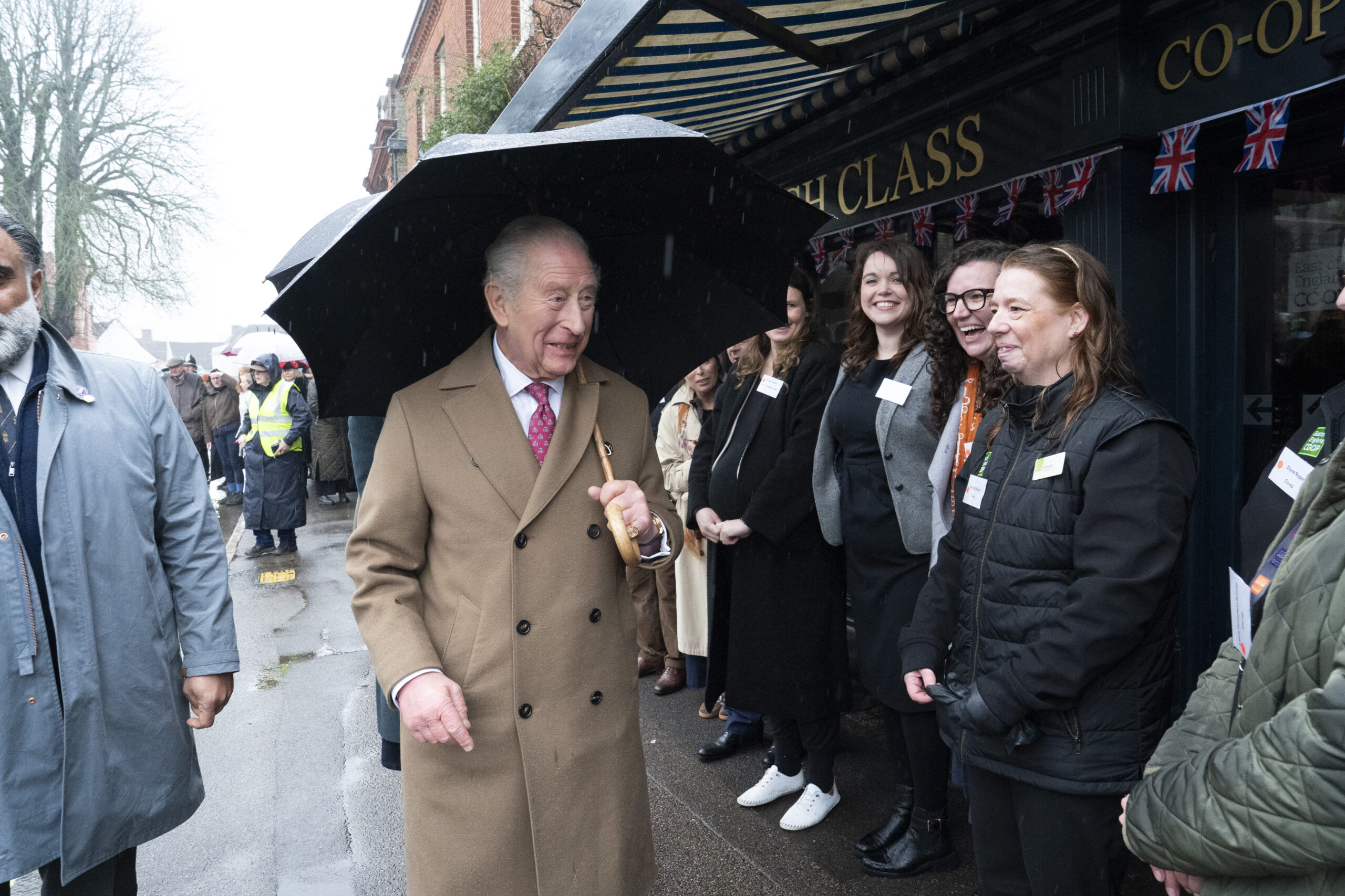 King Charles III, holding an umbrella, greets community heroes in Dedham.